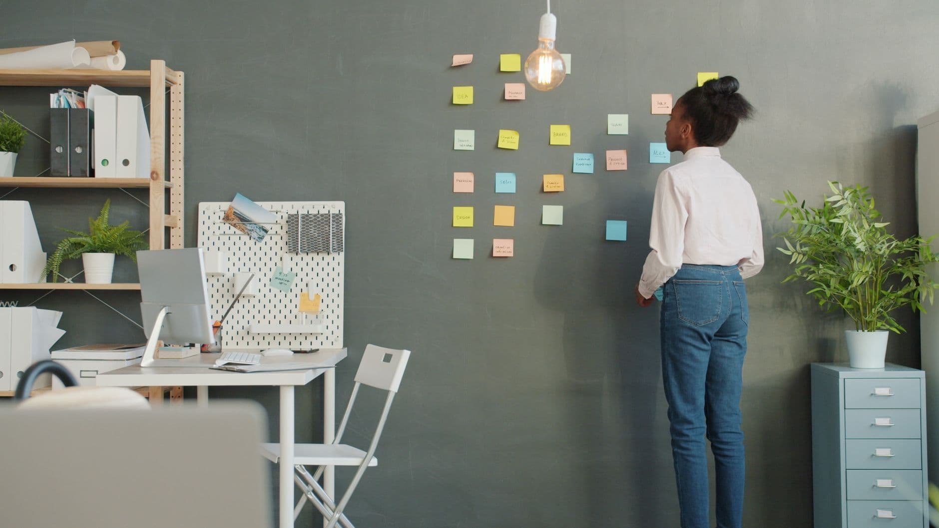 A woman arranging colourful sticky notes on a wall planner