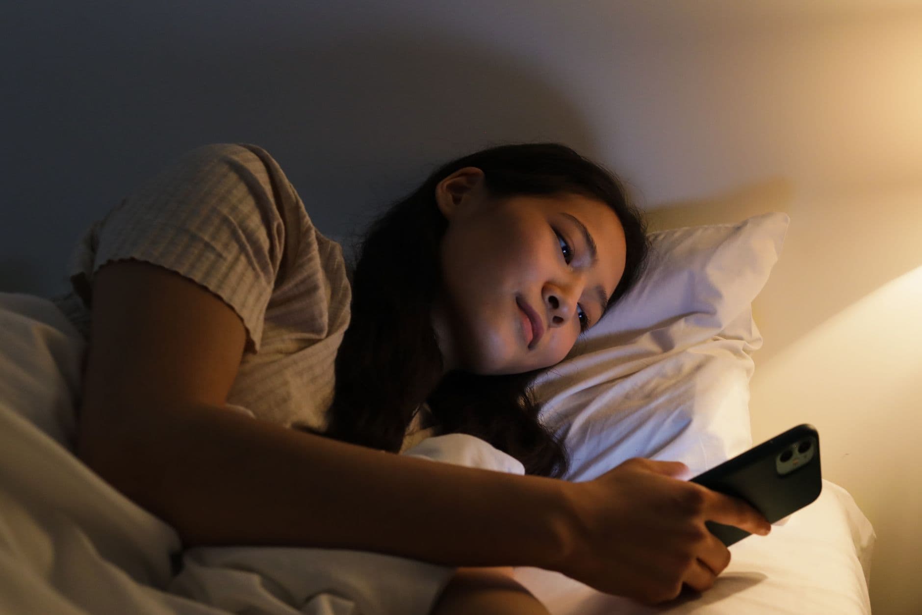 A phone alarm screen glowing on a bedroom bedside table